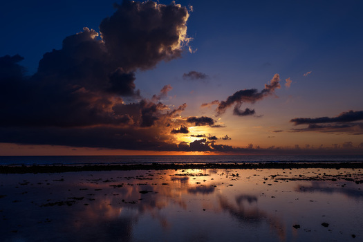 Aerial view of the sun setting behind dark clouds over the Indian Ocean at Mauritius Island with reflections on the water and rocky shore in Mauritius Moka District Mauritius. Aerial view of the sun setting behind dark clouds over the Indian Ocean at Mauritius Island with reflections on the water and rocky shore in Mauritius Moka District Mauritius.