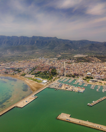Aerial view of a coastal town featuring a large marina sandy beach and rugged mountains in Catalonia Spain. Aerial view of a coastal town featuring a large marina sandy beach and rugged mountains in Catalonia Spain.