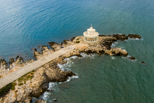 Aerial view of the Saint Theodore Lighthouse a historic white circular structure with columns situated on a rocky peninsula extending into the Ionian Sea in Argostoli Greece.