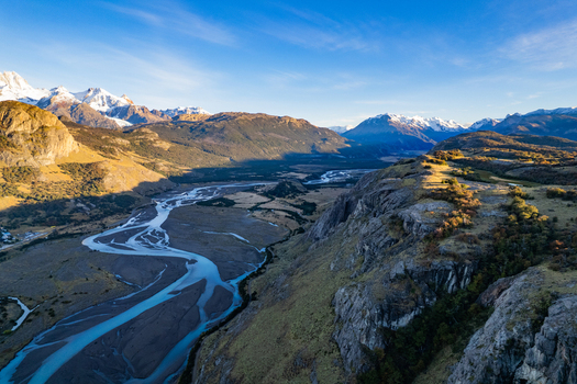 Aerial view of the winding river valley in Patagonia with snow capped mountains rocky cliffs and golden light on the landscape in El Chalten Santa Cruz Argentina. Aerial view of the winding river valley in Patagonia with snow capped mountains rocky cliffs and golden light on the landscape in El Chalten Santa Cruz Argentina.