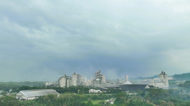 Aerial view of the Nambo cement factory featuring large industrial silos processing structures and chimneys surrounded by lush tropical greenery in Klapanunggal West Java Indonesia. Aerial view of the Nambo cement factory featuring large industrial silos processing structures and chimneys surrounded by lush tropical greenery in Klapanunggal West Java Indonesia.