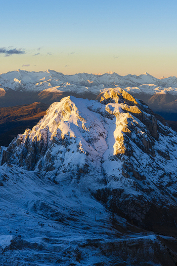 Aerial view of snow capped Puez Odle peaks kissed by the golden light of dawn casting long shadows across the rugged terrain Trentino South Tyrol Italy.