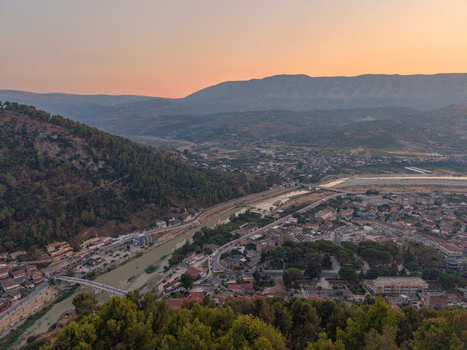 Aerial view of the historic town of Berat along the Osum River featuring traditional stone houses lush hills and mountains under a soft sunset sky in Berat Berat County Albania. Aerial view of the historic town of Berat along the Osum River featuring traditional stone houses lush hills and mountains under a soft sunset sky in Berat Berat County Albania.