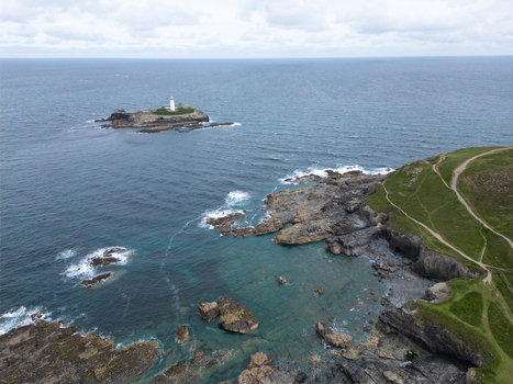 Aerial view of Godrevy Lighthouse on a rocky island surrounded by the blue sea and rugged cliffs with green paths Gwithian England United Kingdom. Aerial view of Godrevy Lighthouse on a rocky island surrounded by the blue sea and rugged cliffs with green paths Gwithian England United Kingdom.
