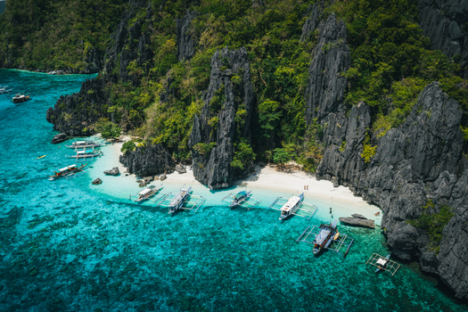 Aerial view of traditional outrigger boats anchored near a white sand beach surrounded by dramatic limestone cliffs and clear turquoise waters in El Nido Mimaropa Philippines. Aerial view of traditional outrigger boats anchored near a white sand beach surrounded by dramatic limestone cliffs and clear turquoise waters in El Nido Mimaropa Philippines.