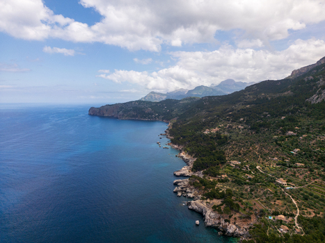 Aerial view of Cala Deia featuring rocky cliffs turquoise Mediterranean waters and lush green hills under a cloudy sky Spain. Aerial view of Cala Deia featuring rocky cliffs turquoise Mediterranean waters and lush green hills under a cloudy sky Spain.