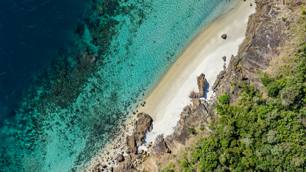 Aerial view of Haslewood Island featuring a pristine white sand beach turquoise coral reef waters and lush coastal vegetation in Whitsundays Queensland Australia. Aerial view of Haslewood Island featuring a pristine white sand beach turquoise coral reef waters and lush coastal vegetation in Whitsundays Queensland Australia.