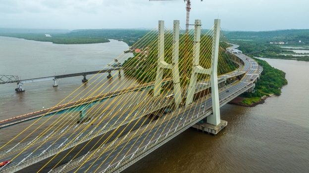 Aerial view of the modern cable stayed Zuari Bridge spanning the river with lush green banks and road traffic in Cortalim Goa India.