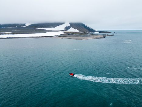 Svalbard and Jan Mayen 28 July 2025 Aerial view of a small red expedition boat cruising through arctic waters near a snow patched coastline under a misty sky. Svalbard and Jan Mayen 28 July 2025 Aerial view of a small red expedition boat cruising through arctic waters near a snow patched coastline under a misty sky.