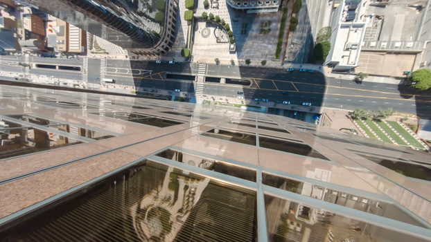 Aerial view of the glass facade of a skyscraper reflecting the city below with streets vehicles and urban infrastructure visible in Downtown Los Angeles California United States.
