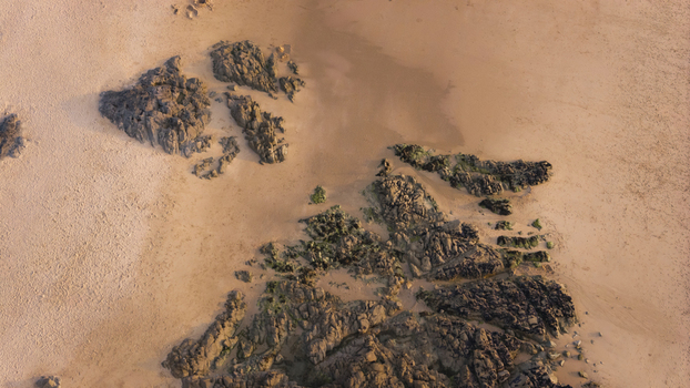 Aerial view of the rugged coastline featuring dark rock formations scattered across the golden sandy beach in Plevenon Brittany France. Aerial view of the rugged coastline featuring dark rock formations scattered across the golden sandy beach in Plevenon Brittany France.