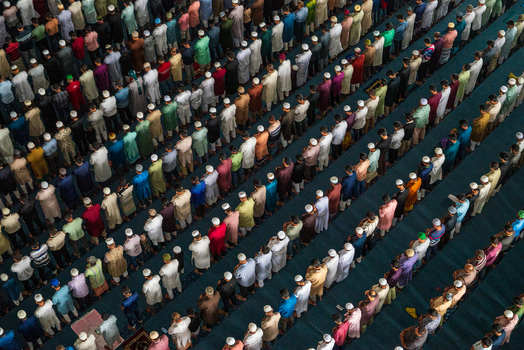 Dhaka Bangladesh 19 June 2026 Aerial view of a large congregation of men praying in organized rows inside a mosque wearing traditional clothing and caps creating a rhythmic pattern.