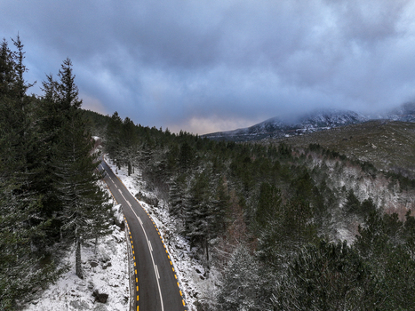 Aerial view of a winding road passing through a snowy pine forest in the Serra da Estrela mountains under a moody winter sky Unhais da Serra Castelo Branco District Portugal. Aerial view of a winding road passing through a snowy pine forest in the Serra da Estrela mountains under a moody winter sky Unhais da Serra Castelo Branco District Portugal.