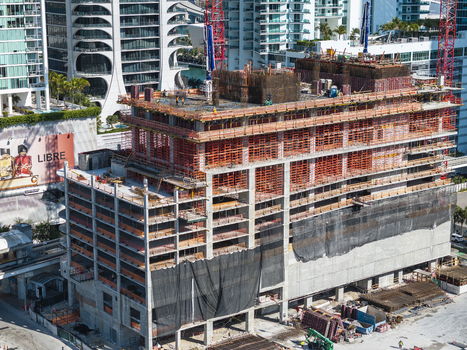 Aerial view of a construction site with cranes rising above the unfinished building against the backdrop of modern high rises and turquoise waters Miami Florida USA. Aerial view of a construction site with cranes rising above the unfinished building against the backdrop of modern high rises and turquoise waters Miami Florida USA.