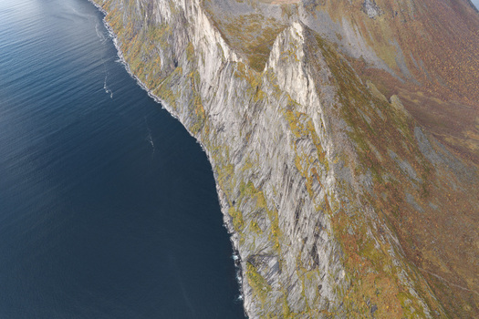 Aerial view of the dramatic rocky cliffs of Senja rising above the deep blue sea showcasing rugged terrain and coastal landscape in Senja Troms Norway.