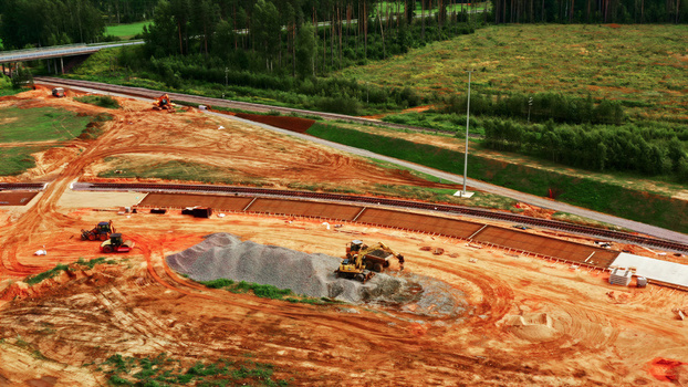 Aerial view of a railway construction site with heavy machinery excavators and piles of gravel near a forest and railway tracks in Latvia. Aerial view of a railway construction site with heavy machinery excavators and piles of gravel near a forest and railway tracks in Latvia.