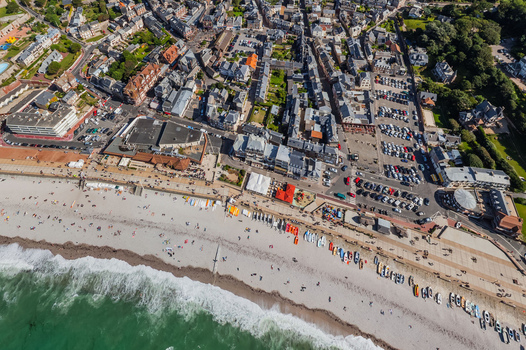 Aerial view of the expansive beach dotted with colorful boats blending into the urban landscape of &Eacute;tretat France.
