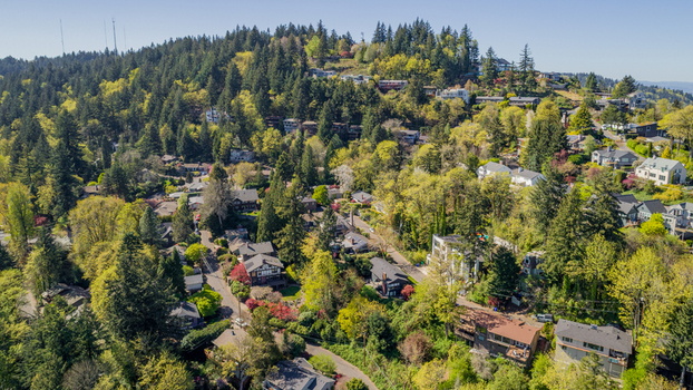 Aerial view of Southwest Imperial Drive residential area with houses nestled among lush green trees on a hillside under a clear sky in Portland Oregon United States. Aerial view of Southwest Imperial Drive residential area with houses nestled among lush green trees on a hillside under a clear sky in Portland Oregon United States.