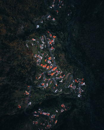 Aerial view of Curral das Freiras nestled in the deep valley of Madeira featuring winding mountain roads traditional houses with orange rooftops and lush surrounding forests in Curral das Freiras Madeira Portugal. Aerial view of Curral das Freiras nestled in the deep valley of Madeira featuring winding mountain roads traditional houses with orange rooftops and lush surrounding forests in Curral das Freiras Madeira Portugal.