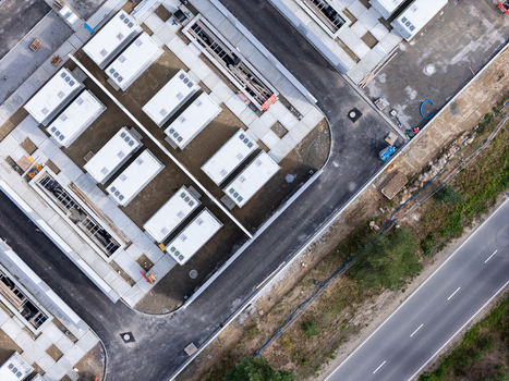 Aerial view of a construction site featuring rows of white modular units paved walkways and an adjacent asphalt road in Poland.