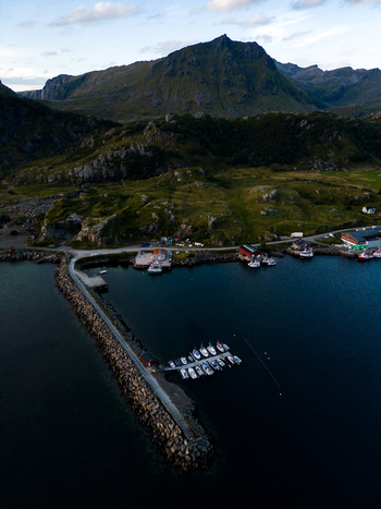 Aerial view of the small harbor of Tangstad with boats docked at a pier and a stone breakwater against a backdrop of rugged mountains and green hills in Leknes Nordland Norway. Aerial view of the small harbor of Tangstad with boats docked at a pier and a stone breakwater against a backdrop of rugged mountains and green hills in Leknes Nordland Norway.