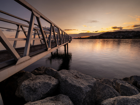 View of Princess Royal Harbour with a metal pier extending into the calm water during a golden sunset in Albany WA Australia. View of Princess Royal Harbour with a metal pier extending into the calm water during a golden sunset in Albany WA Australia.