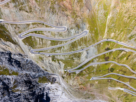 Aerial view of the iconic Stelvio Pass serpentines winding through the rugged alpine landscape with steep rocky slopes and green mountain meadows in Stilfs Trentino Alto Adige Italy.