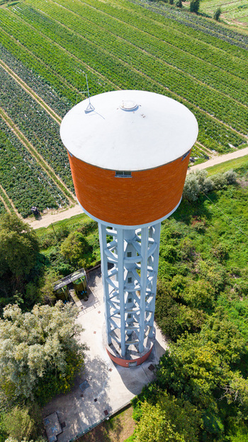 Aerial view of the Torre dell Acquedotto Gruppo CAP water tower with its orange tank and support frame surrounded by agricultural fields in Mediglia Lombardy Italy.