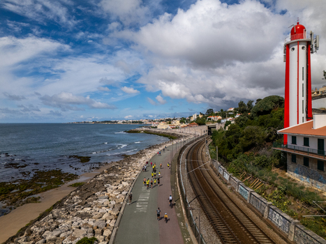 Aerial view of Passeio Maritimo de Alges with people exercising next to a red and white lighthouse and railway tracks along the coast in Cruz Quebrada Lisboa Portugal. Aerial view of Passeio Maritimo de Alges with people exercising next to a red and white lighthouse and railway tracks along the coast in Cruz Quebrada Lisboa Portugal.
