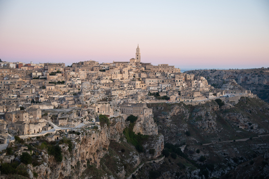 Aerial view of the historic Sassi di Matera stone dwellings and cathedral perched on rocky cliffs during sunset in Matera Basilicata Italy.