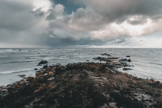 View of the rocky coastline of Vormsi with mossy stones sparse coastal vegetation and a stormy sea under a dramatic cloudy sky Laane County Estonia.