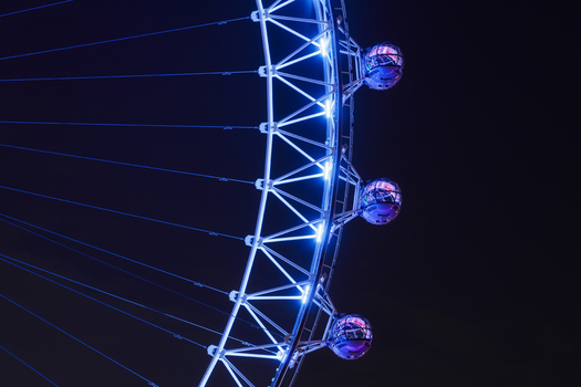 Aerial view of the London Eye illuminated at night with glowing blue passenger capsules and structural steel framework in London Greater London United Kingdom.