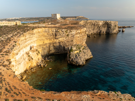 Aerial view of rugged cliffs meet the serene turquoise waters near the iconic St. Mary s Tower a contrast of golden rock and azure sea Blue lagoon Comino Malta. Aerial view of rugged cliffs meet the serene turquoise waters near the iconic St. Mary s Tower a contrast of golden rock and azure sea Blue lagoon Comino Malta.