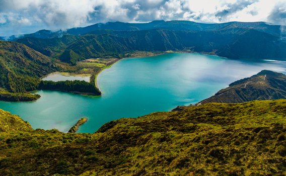 Aerial view of Lagoa do Fogo crater lake with turquoise water surrounded by lush green volcanic mountains under a cloudy sky in Agua de Alto Azores Portugal. Aerial view of Lagoa do Fogo crater lake with turquoise water surrounded by lush green volcanic mountains under a cloudy sky in Agua de Alto Azores Portugal.