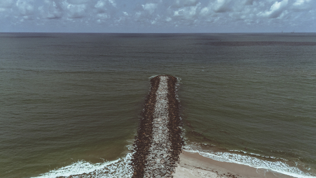 Aerial view of a long stone breakwater extending into the dark ocean waters from a sandy beach under a cloudy sky near Lekki Beach Road in Lekki Lagos Nigeria. Aerial view of a long stone breakwater extending into the dark ocean waters from a sandy beach under a cloudy sky near Lekki Beach Road in Lekki Lagos Nigeria.