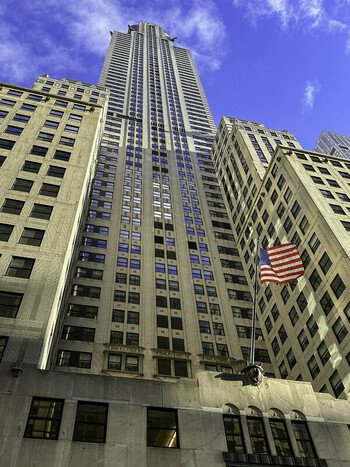 Aerial view of 70 Pine Street an iconic Art Deco skyscraper featuring a prominent American flag against a clear blue sky in the Financial District of New York New York United States.