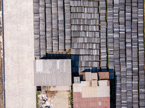Aerial view of an industrial facility with rows of rectangular drying frames in a grid pattern next to a building with a metal roof in Polanharjo Central Java Indonesia.