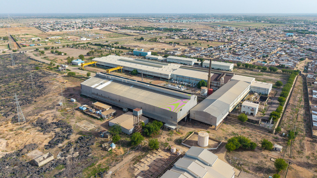 Aerial view of Katsina Steel Rolling Co. Ltd featuring large industrial buildings with metal roofs tall chimneys and surrounding arid landscape in Katsina Katsina Nigeria.