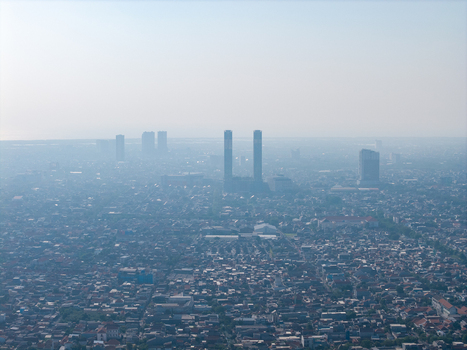 Aerial view of the dense urban sprawl featuring residential rooftops prominent high rise towers and hazy atmospheric conditions in Surabaya East Java Indonesia. Aerial view of the dense urban sprawl featuring residential rooftops prominent high rise towers and hazy atmospheric conditions in Surabaya East Java Indonesia.