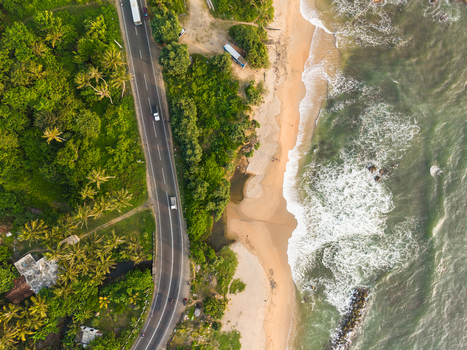 Aerial view of a winding coastal road lined with lush palm trees and a sandy beach with crashing ocean waves Galle Southern Province Sri Lanka.
