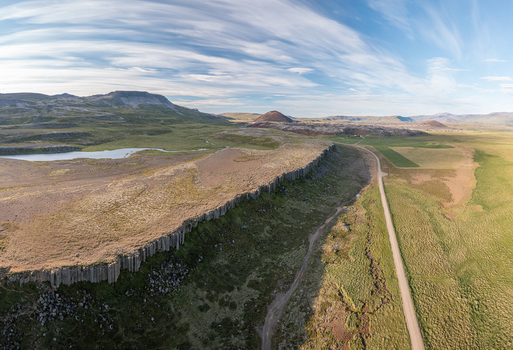 Aerial view of the basalt columns of Gerduberg Cliffs surrounded by green fields and a dirt road in Raudhamelur Eyja og Miklaholtshr Iceland. Aerial view of the basalt columns of Gerduberg Cliffs surrounded by green fields and a dirt road in Raudhamelur Eyja og Miklaholtshr Iceland.