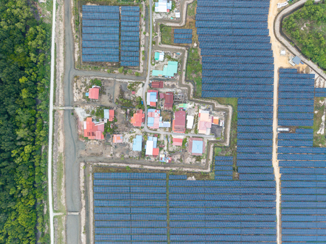 Aerial view of a large scale solar photovoltaic power plant with rows of solar panels surrounding a small residential area and lush green forest in Central Seberang Perai Penang Malaysia. Aerial view of a large scale solar photovoltaic power plant with rows of solar panels surrounding a small residential area and lush green forest in Central Seberang Perai Penang Malaysia.