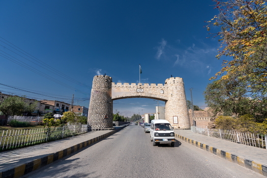 View of the historic Khyber Pass stone archway spanning the road with a white van driving through under a clear blue sky in Khyber District Khyber Pakhtunkhwa Pakistan.