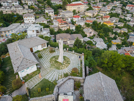Aerial view of the historic old town with stone houses slate roofs and a tall monument in a paved square in Gjirokaster Gjirokaster County Albania. Aerial view of the historic old town with stone houses slate roofs and a tall monument in a paved square in Gjirokaster Gjirokaster County Albania.
