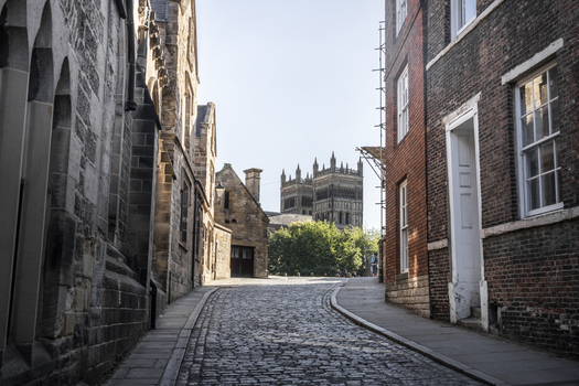 View of the historic Durham Cathedral towers rising above a narrow cobblestone street lined with traditional stone and brick architecture in Durham England United Kingdom. View of the historic Durham Cathedral towers rising above a narrow cobblestone street lined with traditional stone and brick architecture in Durham England United Kingdom.