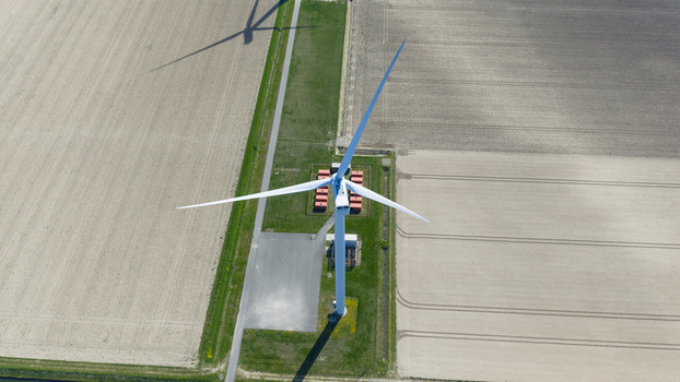Aerial view of a large wind turbine standing in flat agricultural fields with long shadows and service containers Middelharnis South Holland Netherlands. Aerial view of a large wind turbine standing in flat agricultural fields with long shadows and service containers Middelharnis South Holland Netherlands.
