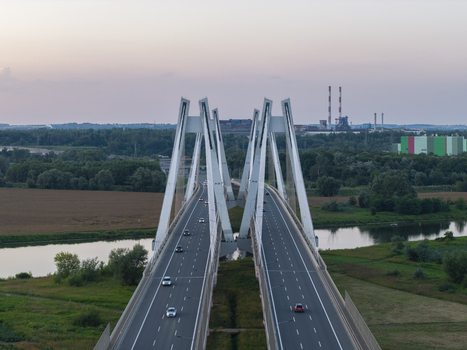 Aerial view of the Most na S7 cable stayed bridge spanning the Vistula River with traffic surrounded by green fields and industrial structures in Krakow Malopolskie Poland. Aerial view of the Most na S7 cable stayed bridge spanning the Vistula River with traffic surrounded by green fields and industrial structures in Krakow Malopolskie Poland.