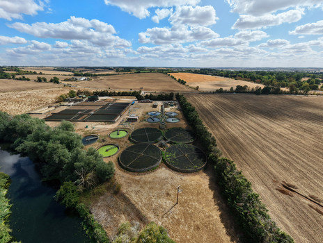 Aerial view of the wastewater treatment works featuring circular sedimentation tanks and rectangular treatment beds near a river and agricultural fields in St Neots England United Kingdom. Aerial view of the wastewater treatment works featuring circular sedimentation tanks and rectangular treatment beds near a river and agricultural fields in St Neots England United Kingdom.