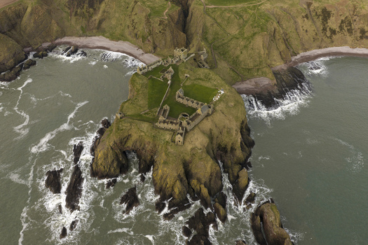 Aerial view of Dunnottar Castle situated on a dramatic rocky headland surrounded by the North Sea and green cliffs in Stonehaven Scotland United Kingdom. Aerial view of Dunnottar Castle situated on a dramatic rocky headland surrounded by the North Sea and green cliffs in Stonehaven Scotland United Kingdom.