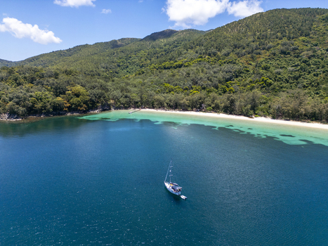 Aerial view of a sailboat anchored in turquoise waters near a white sand beach and lush tropical hills in Guanaja Bay Islands Department Honduras. Aerial view of a sailboat anchored in turquoise waters near a white sand beach and lush tropical hills in Guanaja Bay Islands Department Honduras.